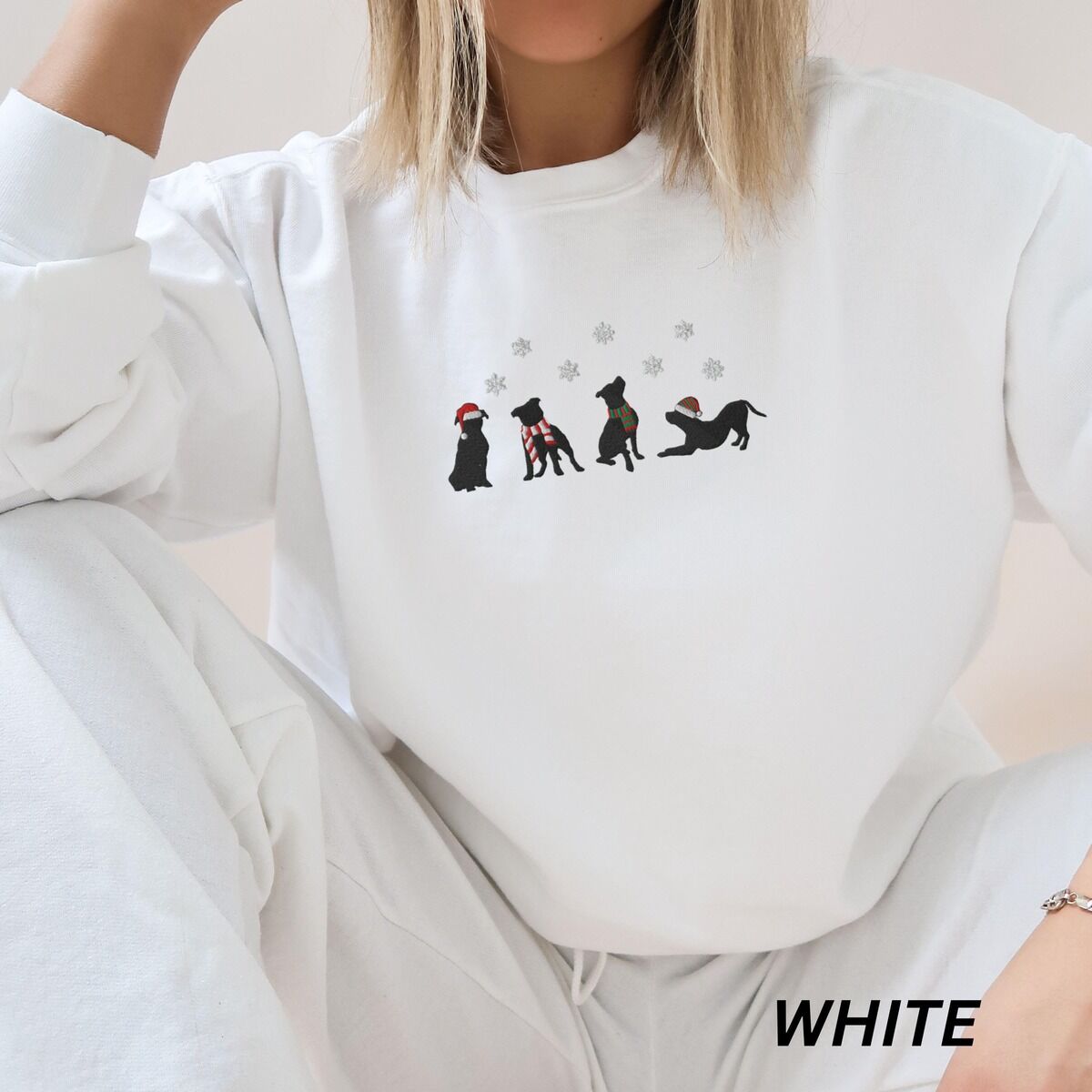 Pitbull Silhouette Christmas Sweatshirt – White Woman in a White crewneck sweatshirt and matching sweatpants, embroidered with four black pitbull silhouettes in a Santa hat, striped scarves and a knit hat under snowflakes