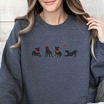 Smiling woman in a Dark Heather crewneck sweatshirt embroidered with four black pitbull silhouettes with red bandanas, a red heart headband and a floating red heart