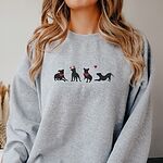 Smiling woman in a Sport Grey crewneck sweatshirt embroidered with four black pitbull silhouettes with red bandanas, a red heart headband and a floating red heart