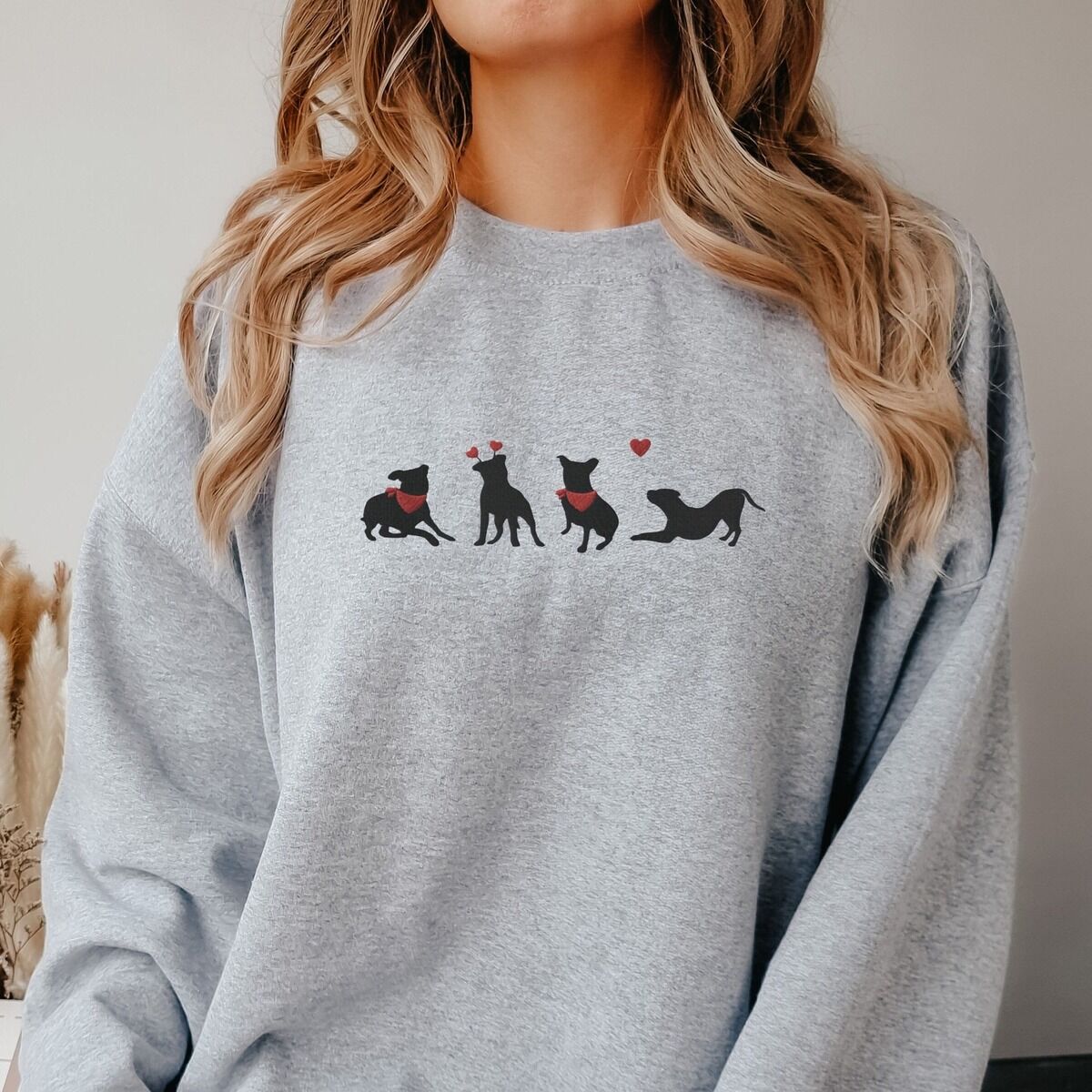 Pitbull Valentine Sweatshirt - worn Smiling woman in a Sport Grey crewneck sweatshirt embroidered with four black pitbull silhouettes with red bandanas, a red heart headband and a floating red heart