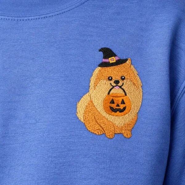 Close-up of the embroidered Pomeranian in a witch hat holding a jack-o'-lantern bucket on the left chest of a Heather Deep Royal sweatshirt