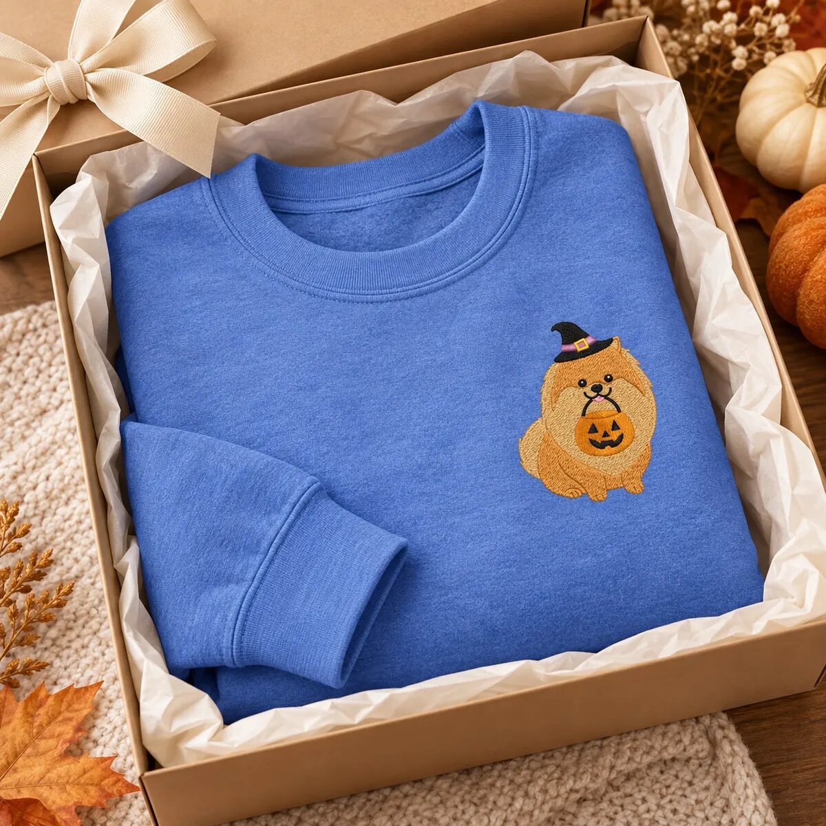 Pomeranian Halloween Sweatshirt in a Gift Box Pomeranian Halloween sweatshirt in Heather Deep Royal folded in a kraft gift box with a ribbon, pumpkins and autumn leaves