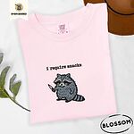 Blossom Comfort Colors T-shirt embroidered with a feral raccoon holding a little knife under the words i require snacks embroidered on the chest