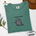 Light Green Comfort Colors T-shirt embroidered with a feral raccoon holding a little knife under the words i require snacks embroidered on the chest