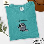 Seafoam Comfort Colors T-shirt embroidered with a feral raccoon holding a little knife under the words i require snacks embroidered on the chest