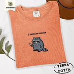 Terracotta Comfort Colors T-shirt embroidered with a feral raccoon holding a little knife under the words i require snacks embroidered on the chest