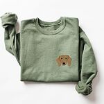 Military Green crewneck sweatshirt laid flat on white, embroidered with a red dachshund face with long floppy ears, round black eyes and a little smile on the left chest
