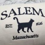 Close-up of the black Salem Massachusetts embroidery with arched SALEM letters over a walking black cat