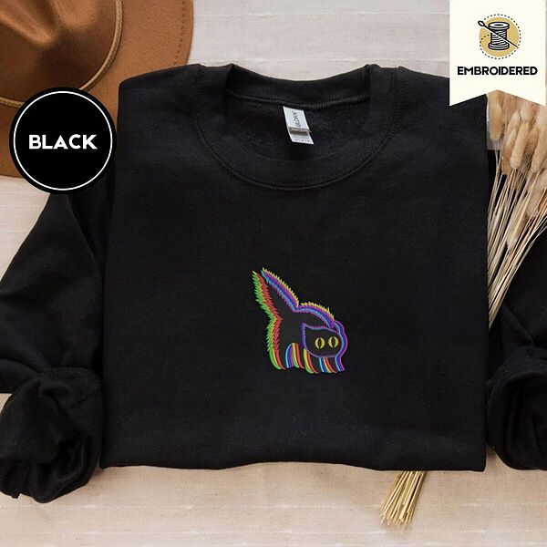 Black crewneck sweatshirt with a brown felt hat and dried bunny tail grass, embroidered with a startled black cat with an arched back, a puffed tail and yellow eyes, outlined in layered rainbow neon stitches