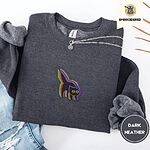 Dark Heather crewneck sweatshirt folded with ripped jeans and a silver chain necklace, embroidered with a startled black cat with an arched back, a puffed tail and yellow eyes, outlined in layered rainbow neon stitches