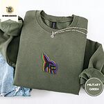Military Green crewneck sweatshirt folded with light jeans and a silver chain necklace, embroidered with a startled black cat with an arched back, a puffed tail and yellow eyes, outlined in layered rainbow neon stitches