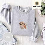 Ash crewneck sweatshirt folded with denim shorts, white sneakers and a potted plant, embroidered with a gold and white Shih Tzu puppy with a long silky coat and a plumed tail