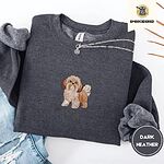 Dark Heather crewneck sweatshirt folded with ripped jeans and a silver chain necklace, embroidered with a gold and white Shih Tzu puppy with a long silky coat and a plumed tail