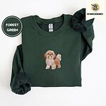 Forest Green crewneck sweatshirt folded on a white background, embroidered with a gold and white Shih Tzu puppy with a long silky coat and a plumed tail