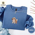 Indigo Blue crewneck sweatshirt folded with light jeans and dried twigs, embroidered with a gold and white Shih Tzu puppy with a long silky coat and a plumed tail