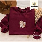 Maroon crewneck sweatshirt with a brown felt hat and dried bunny tail grass, embroidered with a gold and white Shih Tzu puppy with a long silky coat and a plumed tail