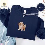 Navy crewneck sweatshirt folded with ripped jeans and a silver chain necklace, embroidered with a gold and white Shih Tzu puppy with a long silky coat and a plumed tail