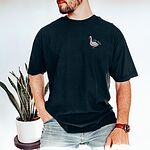 Man leaning on a stool beside a snake plant in a Black T-shirt embroidered with a white goose and the words silly dada