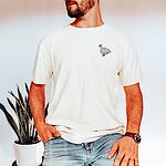 Man in an Ivory T-shirt and jeans beside a snake plant, embroidered with a white goose and the words silly dada