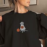 Woman in a Black crewneck sweatshirt embroidered with a silver lab in a white ghost sheet holding a jack-o'-lantern bucket