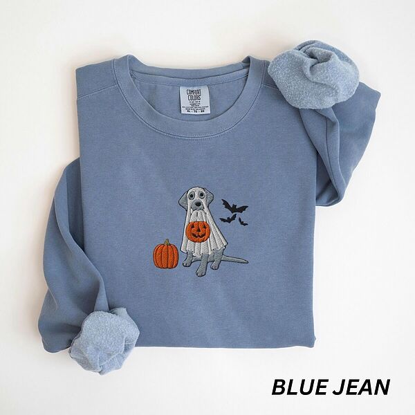 Blue Jean crewneck sweatshirt laid flat with rolled cuffs, embroidered with a silver Labrador in a white ghost sheet holding a jack-o'-lantern bucket beside a pumpkin and three bats