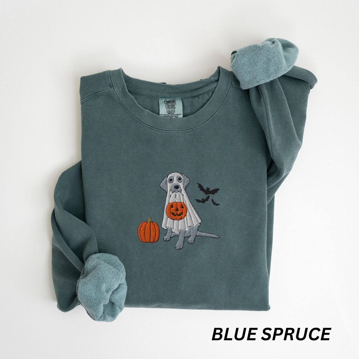 Silver Lab Ghost Sweatshirt – Blue Spruce Blue Spruce crewneck sweatshirt laid flat with rolled cuffs, embroidered with a silver lab in a ghost costume, an orange pumpkin and bats