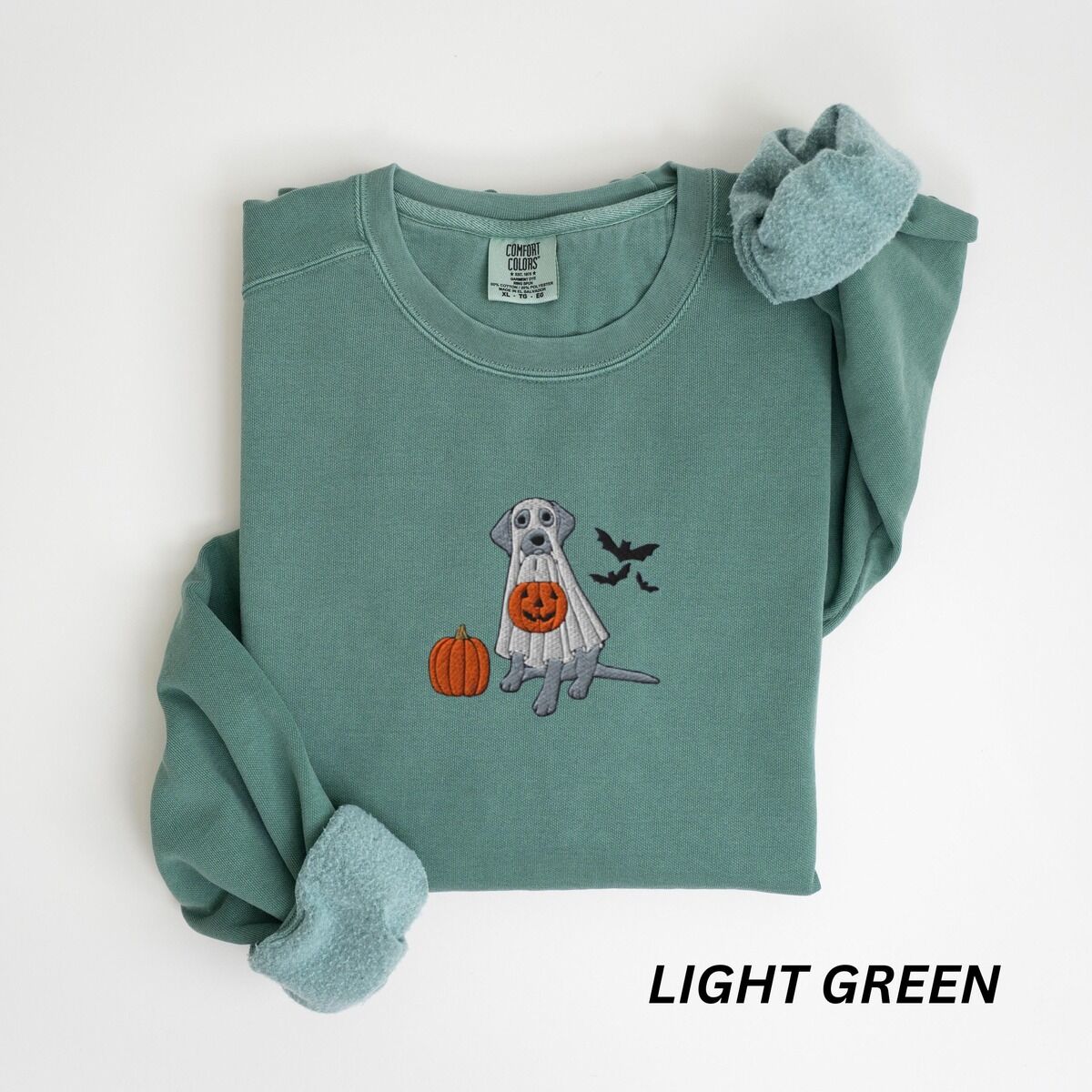 Silver Lab Ghost Sweatshirt – Light Green Light Green crewneck sweatshirt laid flat, embroidered with a silver lab trick-or-treating in a ghost sheet beside a pumpkin and bats