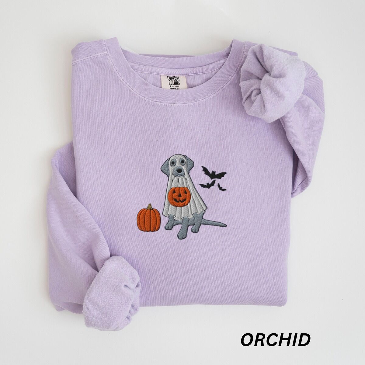 Silver Lab Ghost Sweatshirt – Orchid Orchid crewneck sweatshirt laid flat, embroidered with a silver Labrador in a white ghost sheet holding a jack-o'-lantern bucket beside a pumpkin and three bats
