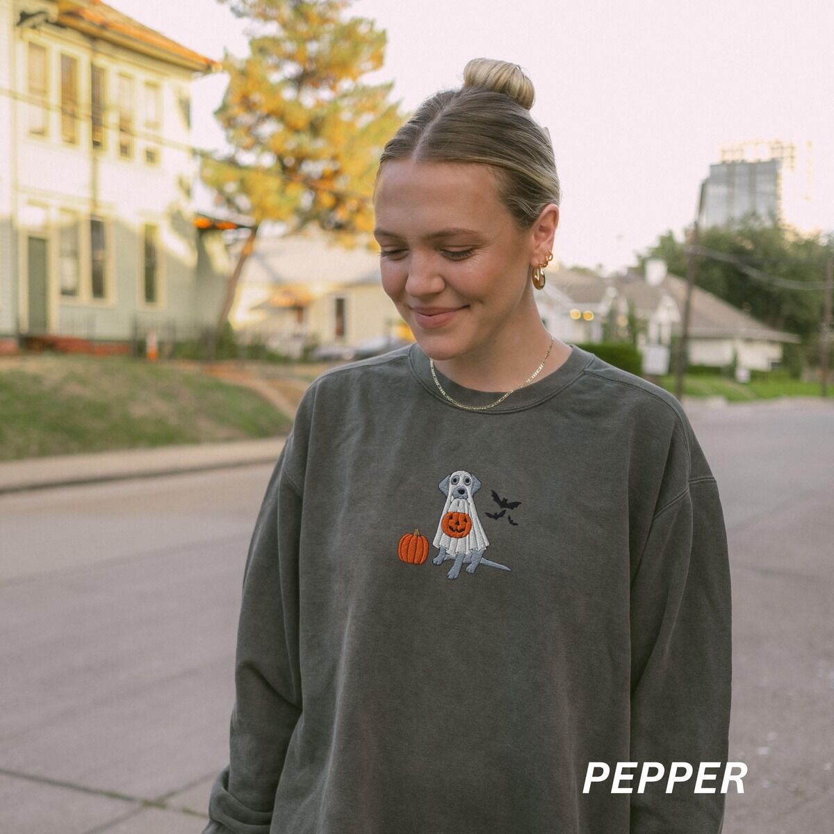 Silver Lab Ghost Sweatshirt – Pepper Woman on a street in a Pepper crewneck sweatshirt embroidered with a silver lab in a ghost costume holding a jack-o'-lantern bucket
