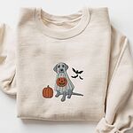 Sand crewneck sweatshirt laid flat on a white background, embroidered with a silver Labrador in a white ghost sheet holding a jack-o'-lantern bucket beside a pumpkin and three bats