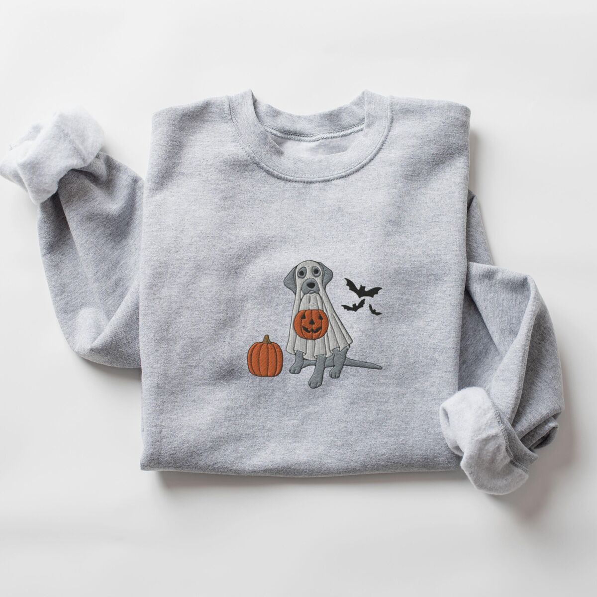 Silver Lab Ghost Sweatshirt - Sport Grey Sport Grey crewneck sweatshirt laid flat with rolled cuffs, embroidered with a silver lab trick-or-treating in a ghost sheet beside an orange pumpkin and bats