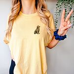 Woman making a peace sign in a Butter T-shirt embroidered with a small sitting golden retriever on the left chest
