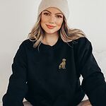 Woman in a beanie and a Black crewneck sweatshirt embroidered with a small sitting golden retriever on the left chest