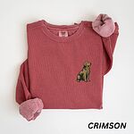 Crimson crewneck sweatshirt laid flat, embroidered with a small sitting golden retriever on the left chest