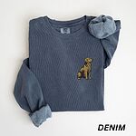 Denim crewneck sweatshirt laid flat, embroidered with a small sitting golden retriever on the left chest