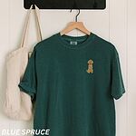 Blue Spruce T-shirt on a hanger beside a canvas tote, embroidered with a small golden goldendoodle sitting on the left chest