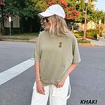 Woman in a cap on a city street in a Khaki T-shirt embroidered with a small golden goldendoodle sitting on the left chest