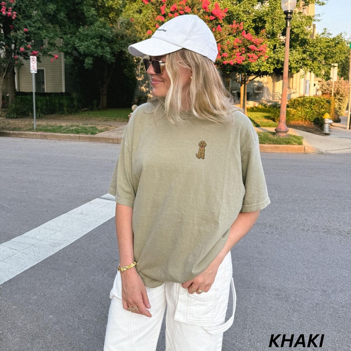 Sitting Goldendoodle Shirt – Khaki Woman in a cap on a city street in a Khaki T-shirt embroidered with a small golden goldendoodle sitting on the left chest