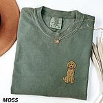Moss T-shirt laid flat with a hat and a necklace, embroidered with a small golden goldendoodle sitting on the left chest