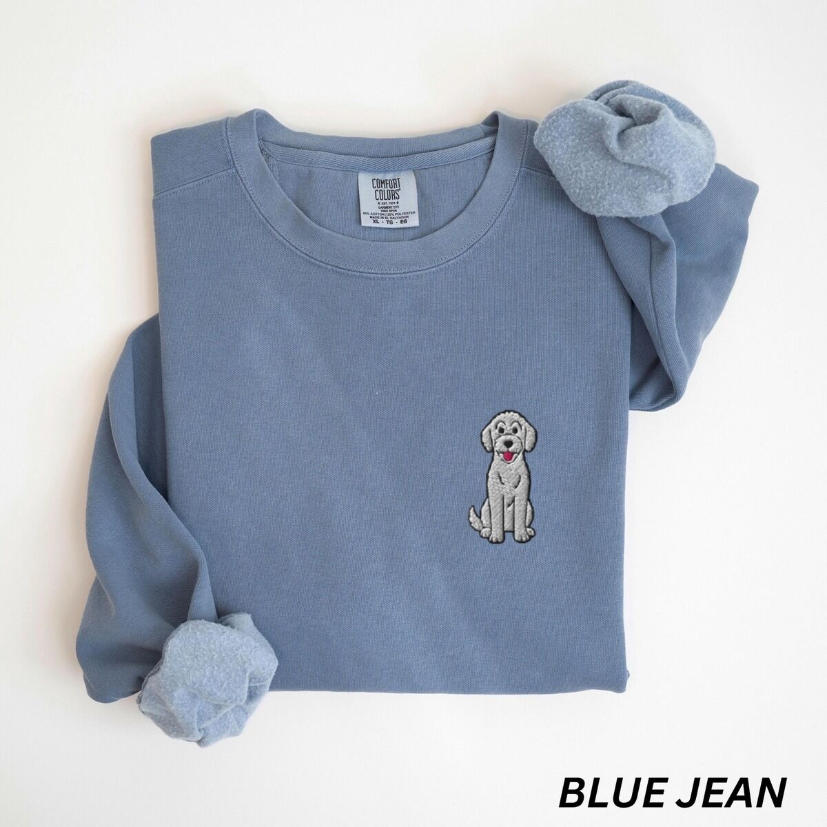 Sitting Goldendoodle Sweatshirt – Blue Jean Blue Jean crewneck sweatshirt laid flat, embroidered with a small light grey goldendoodle sitting on the left chest