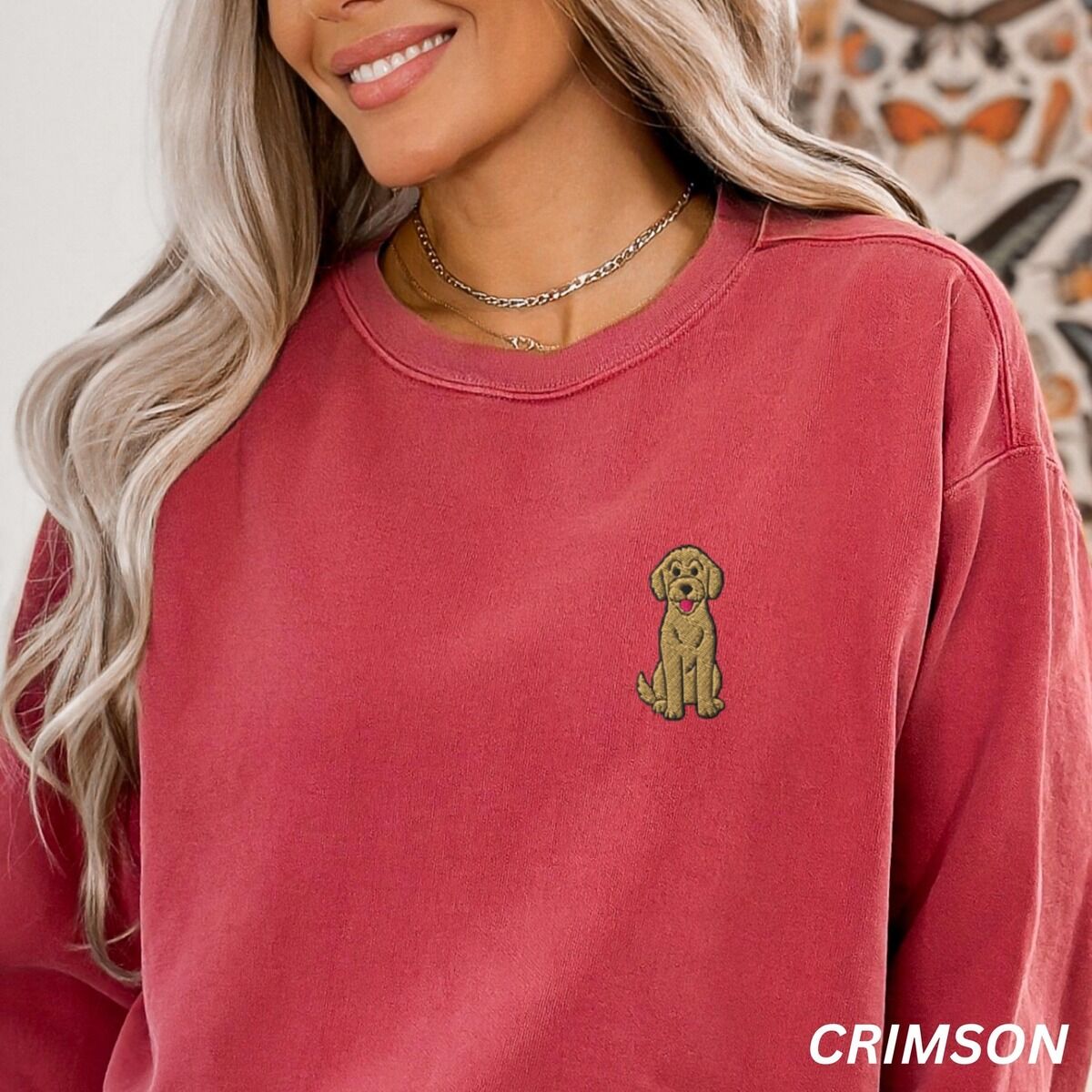 Sitting Goldendoodle Sweatshirt – Crimson Smiling woman in a Crimson crewneck sweatshirt embroidered with a small golden goldendoodle sitting on the left chest