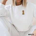 Woman in a White crewneck sweatshirt and white joggers, embroidered with a small golden goldendoodle sitting on the left chest