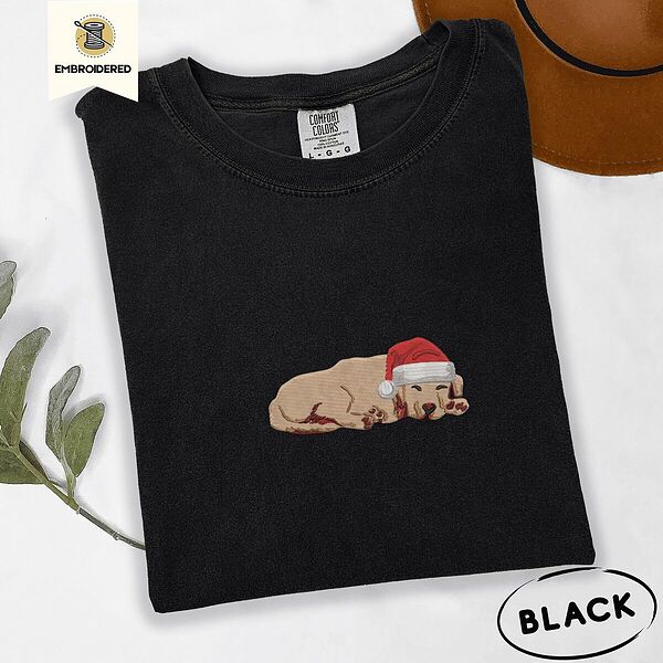 Black Comfort Colors T-shirt embroidered with a golden retriever puppy napping with its head on its paws in a red Santa hat