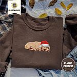 Dark Chocolate crewneck sweatshirt on a plaid flannel shirt with yellow autumn leaves and denim shorts, embroidered with a golden retriever puppy asleep in a red Santa hat, its head resting on its front paws