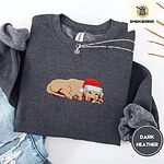 Dark Heather crewneck sweatshirt folded with ripped jeans and a silver chain necklace, embroidered with a golden retriever puppy asleep in a red Santa hat, its head resting on its front paws