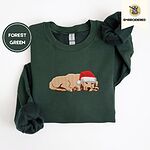 Forest Green crewneck sweatshirt folded on a white background, embroidered with a golden retriever puppy asleep in a red Santa hat, its head resting on its front paws
