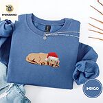 Indigo Blue crewneck sweatshirt folded with light jeans and dried twigs, embroidered with a golden retriever puppy asleep in a red Santa hat, its head resting on its front paws