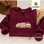 Maroon crewneck sweatshirt with a brown felt hat and dried bunny tail grass, embroidered with a golden retriever puppy asleep in a red Santa hat, its head resting on its front paws