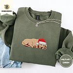 Military Green crewneck sweatshirt folded with light jeans and a silver chain necklace, embroidered with a golden retriever puppy asleep in a red Santa hat, its head resting on its front paws