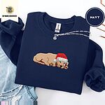 Navy crewneck sweatshirt folded with ripped jeans and a silver chain necklace, embroidered with a golden retriever puppy asleep in a red Santa hat, its head resting on its front paws